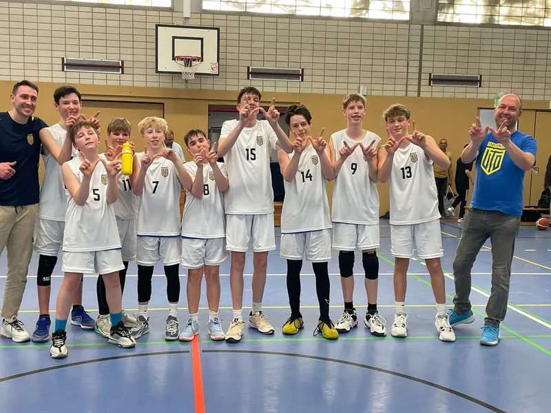A United Basketball youth team in white shirts makes a hand sign with the coaches after a game in Berlin.