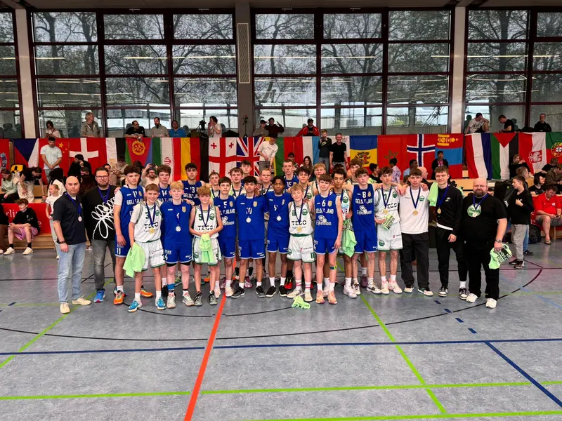United Basketball players and staff with their medals in a sports hall in Berlin, with the flags of the participating countries behind them.