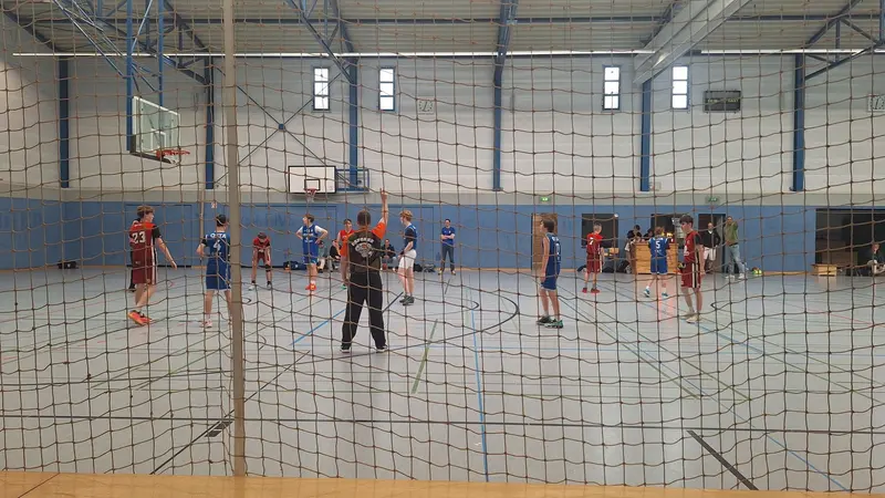 A United Basketball youth team in blue plays a team in red, seen through the net beside the court, at the tournament in Leer.