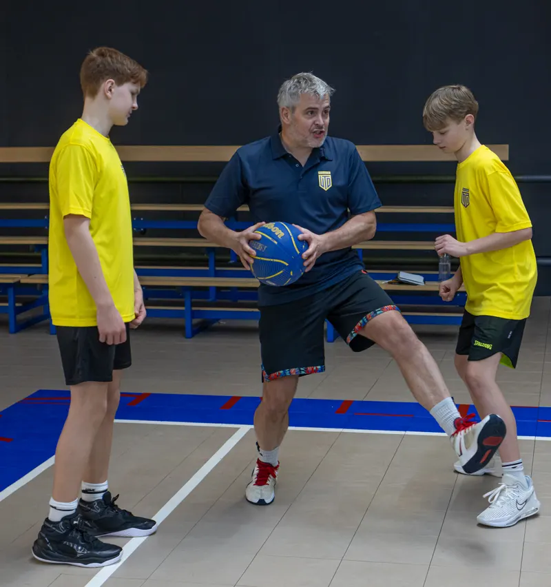 Een trainer doet een dribbelbeweging voor aan twee jeugdspelers