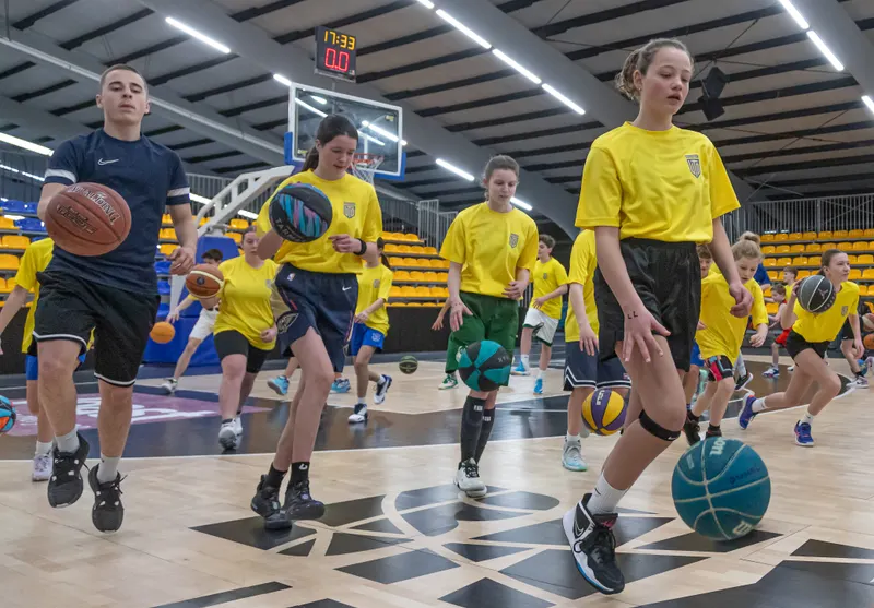 Een volle zaal kinderen dribbelt tegelijk met een bal tijdens het Skills Camp in De Kooi